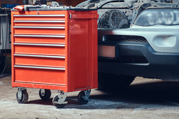 Photo of a large red tool chest on wheels, in front of a car in a garage.